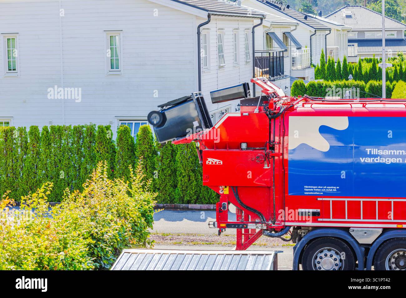 Poubelle noire soulevée par le système automatisé de camion à ordures rouge bleu lors de l'élimination des déchets dans la zone résidentielle. Suède. Uppsala. Banque D'Images