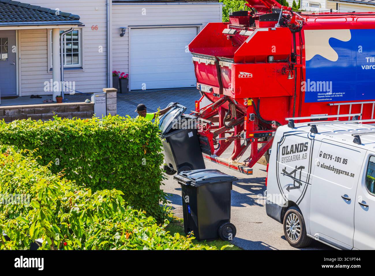 Travailleur attache des poubelles noires à camion à ordures automatisé dans le quartier de villa européenne. Suède. Uppsala. Banque D'Images