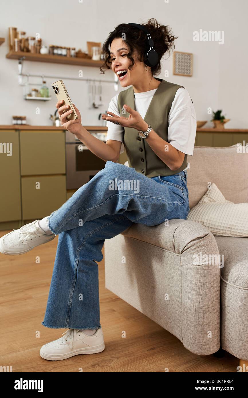 Une jeune femme joyeuse étudie à la maison, s'engageant joyeusement avec son téléphone. Banque D'Images