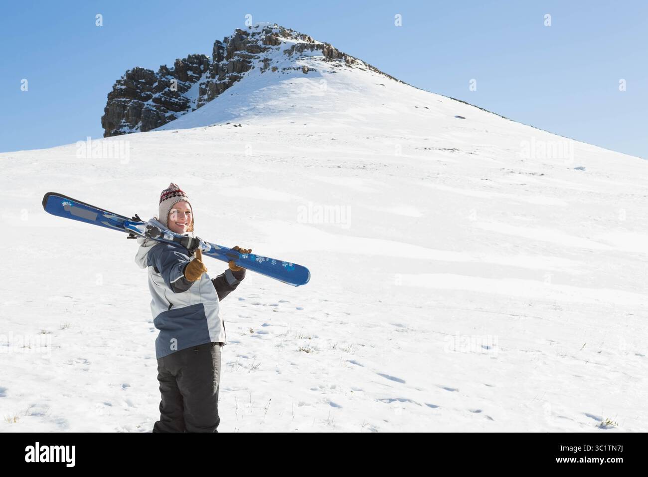 Femme portant une paire de skis alpins sur l'épaule portant veste de ski sur une pente enneigée, espace copie Banque D'Images