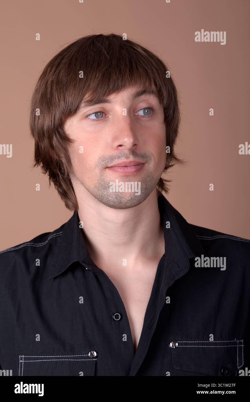 Un jeune homme aux cheveux élégants se tient confiant, engageant le spectateur. Banque D'Images