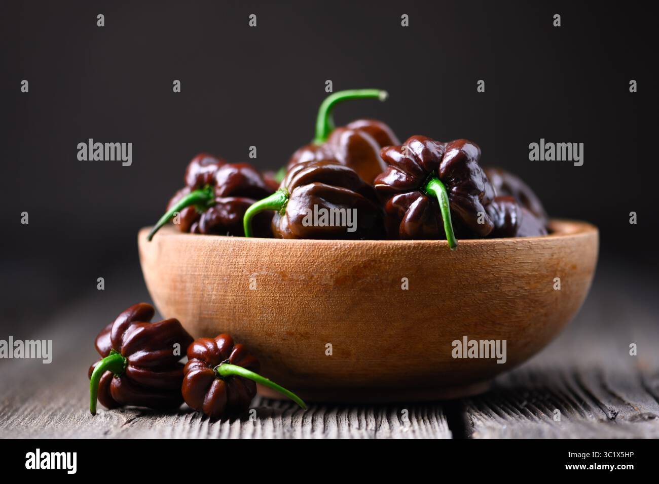 Poivrons habanero au chocolat mûrs (capsicum chinense) dans un bol en bois sur une table rustique. Les poivrons mexicains très chauds se rapprochent Banque D'Images