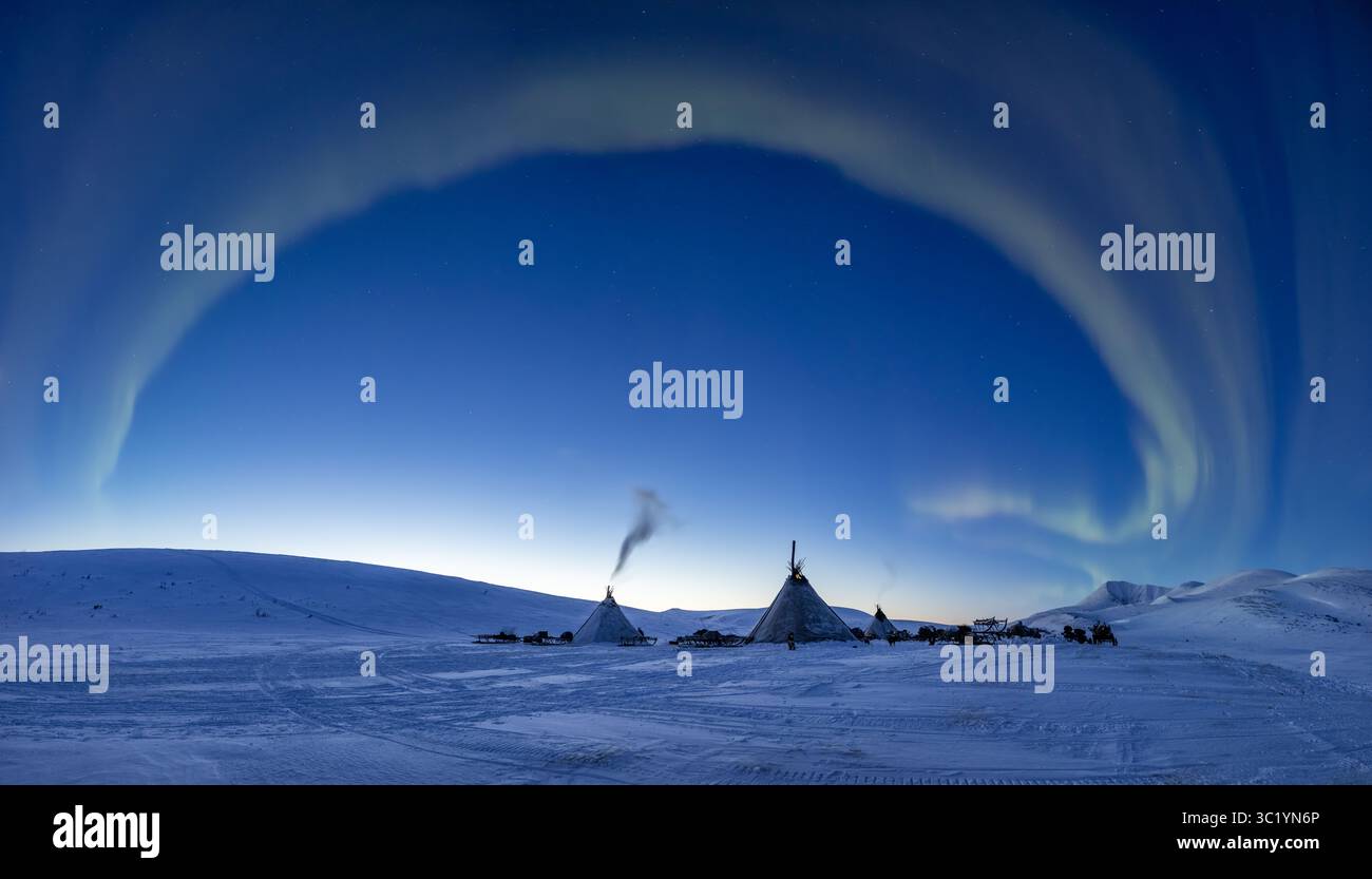 Vue de l'aurore boréale éthérée peint le ciel au-dessus des habitations coniques traditionnelles sur la toundra enneigée, une danse de lumière et d'ombre, Salekhard, Okrug autonome Yamalo-Nenets, Russie. Banque D'Images