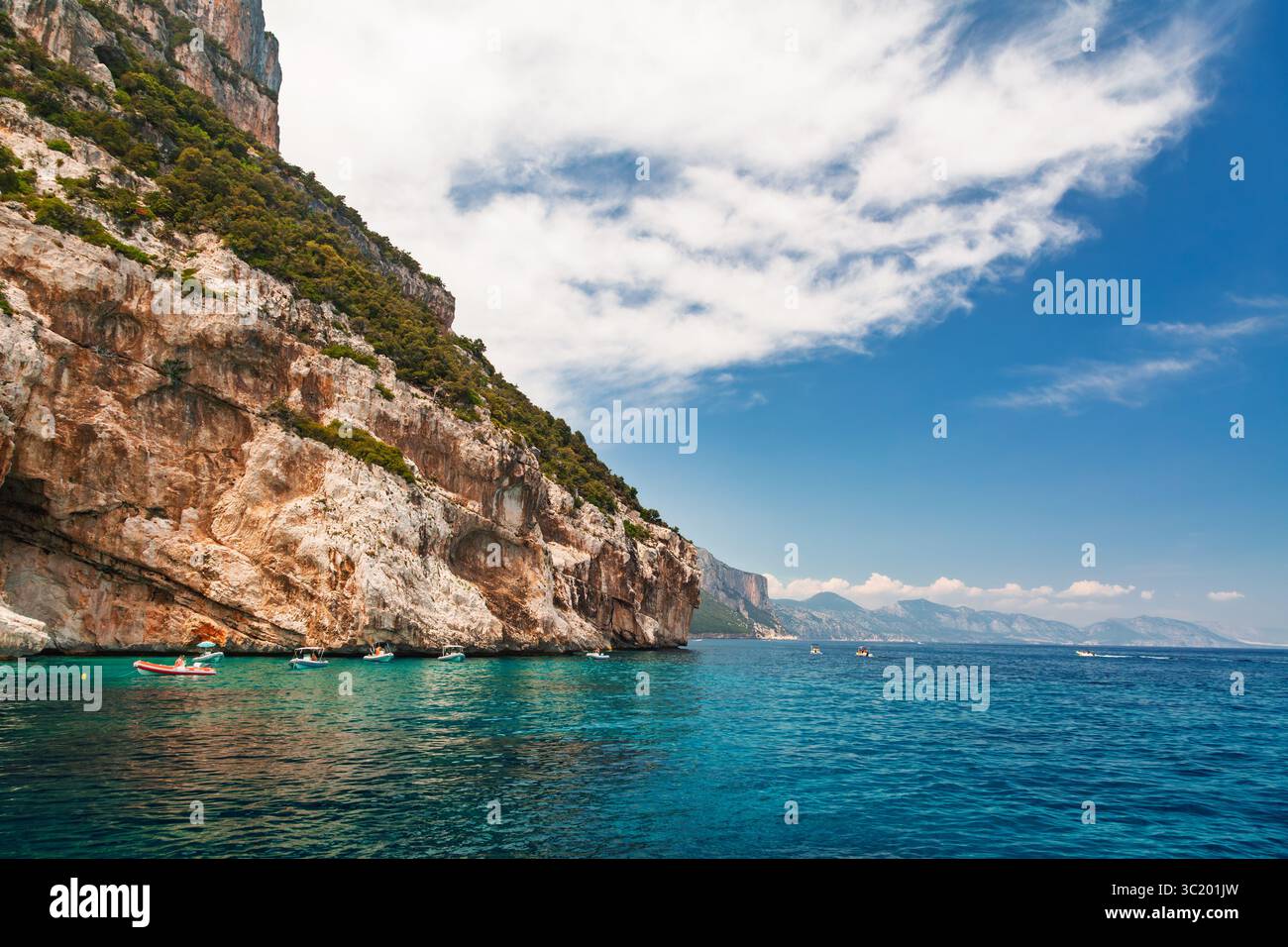 Les bateaux flottent près de la côte turquoise sous les falaises abruptes et boisées le long du golfe d'Orosei sur la côte orientale de la Sardaigne en été Banque D'Images