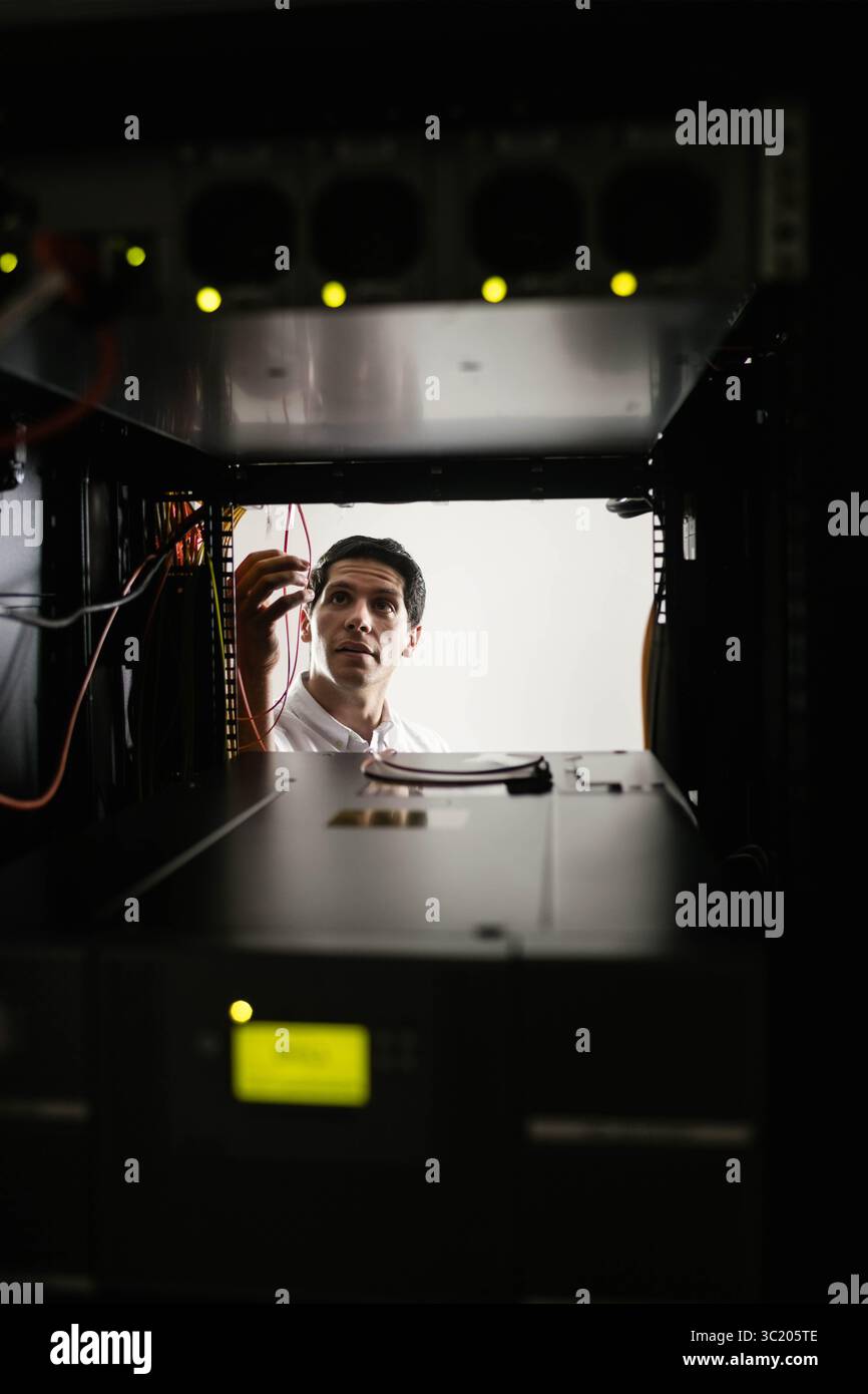 Technicien INFORMATIQUE de sexe masculin ajustant les câbles Ethernet à l'intérieur du rack de serveur au centre de données avec des voyants clignotants Banque D'Images