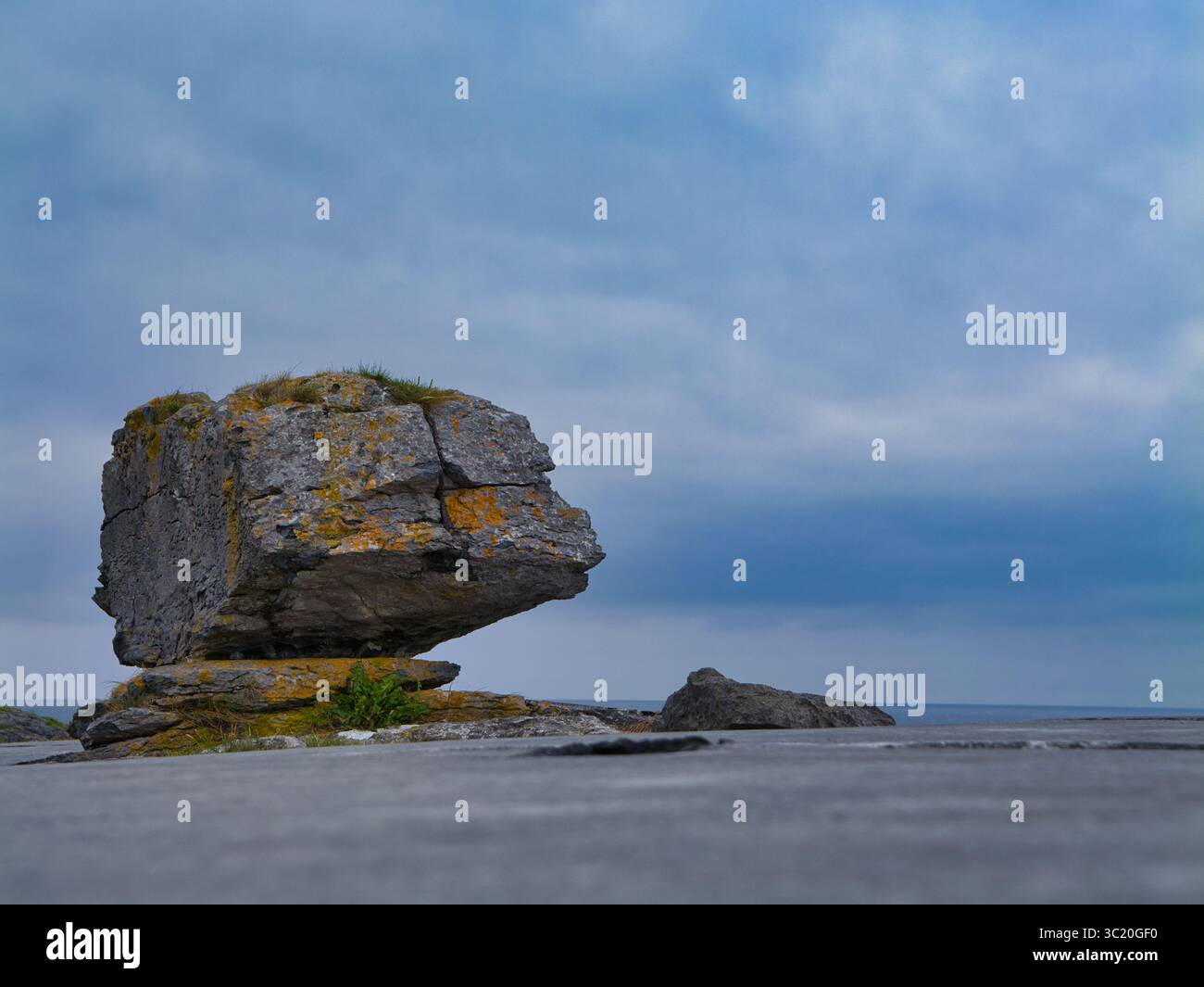 Une erratique saisissante se dresse sur le trottoir de calcaire accidenté du Burren, en Irlande, sous un ciel sombre. Banque D'Images