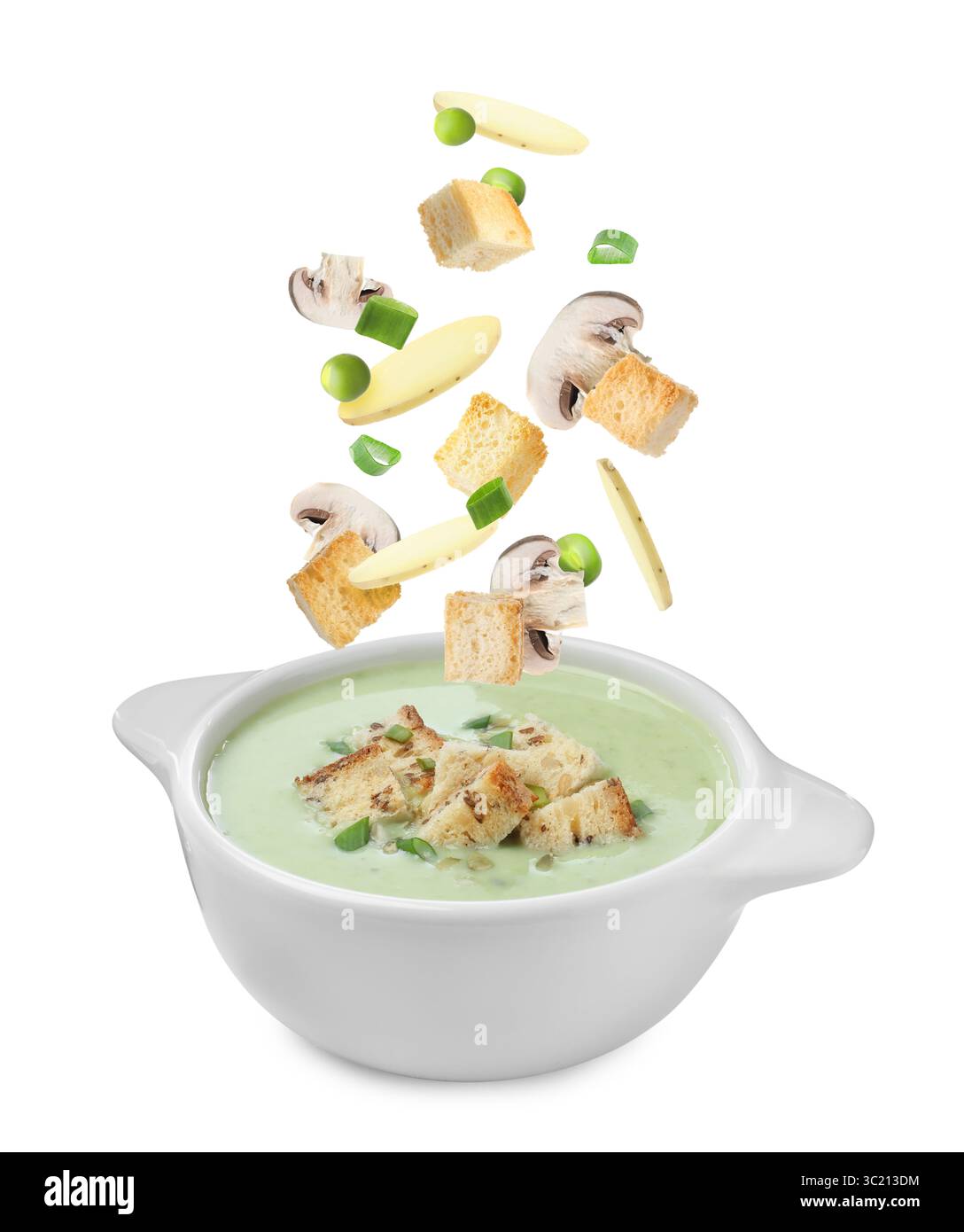 Croûtons, champignons et tranches de pommes de terre tombant dans un bol de soupe sur fond blanc Banque D'Images