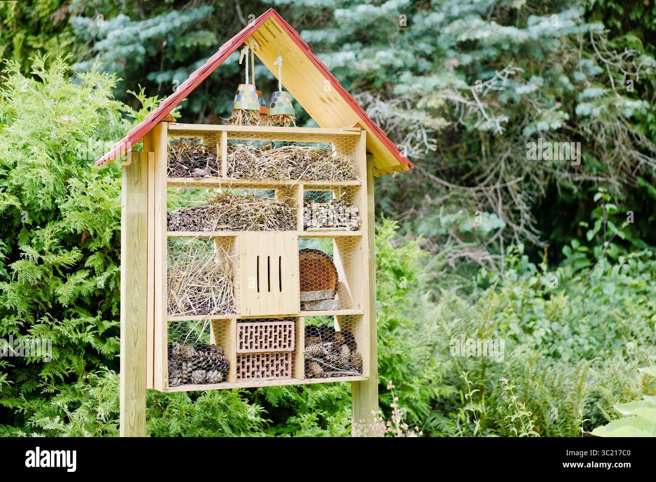 Hôtel d'insectes en bois dans un jardin, rempli de pommes de pin, de paille et de brindilles - un abri pour les pollinisateurs et les insectes bénéfiques. Banque D'Images