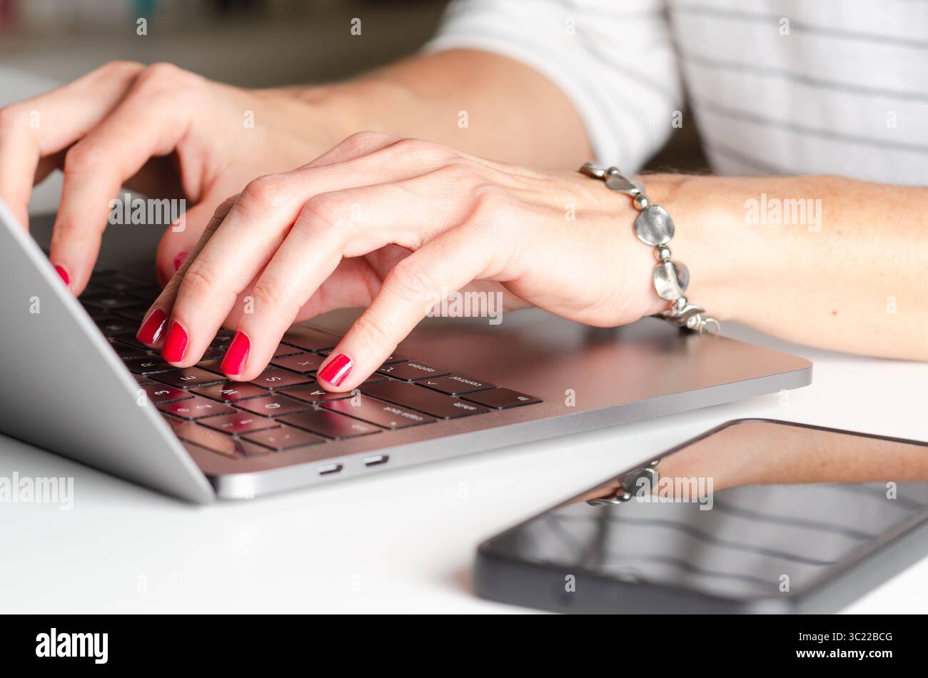 Mains d'une femme avec des ongles peints en rouge dans un bureau à l'aide d'un ordinateur portable et d'un téléphone portable. Les femmes dans le concept d'entreprise. Banque D'Images