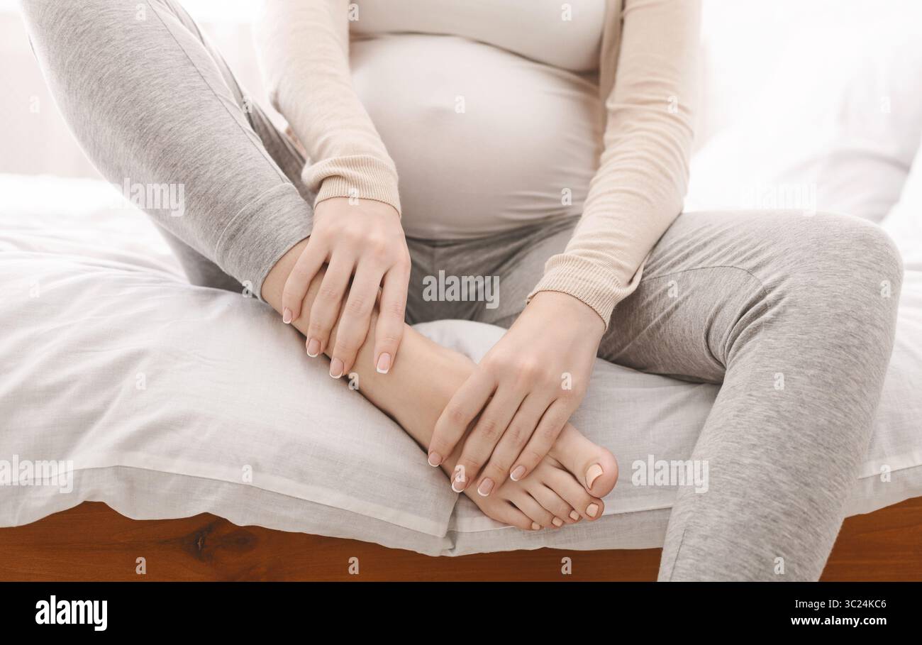 Femme enceinte en massant son pied enflé sitting on bed Banque D'Images