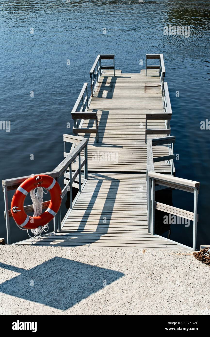 Quai en bois s'étendant au-dessus de l'eau calme avec une bouée de sauvetage dans un cadre serein au bord du lac Banque D'Images