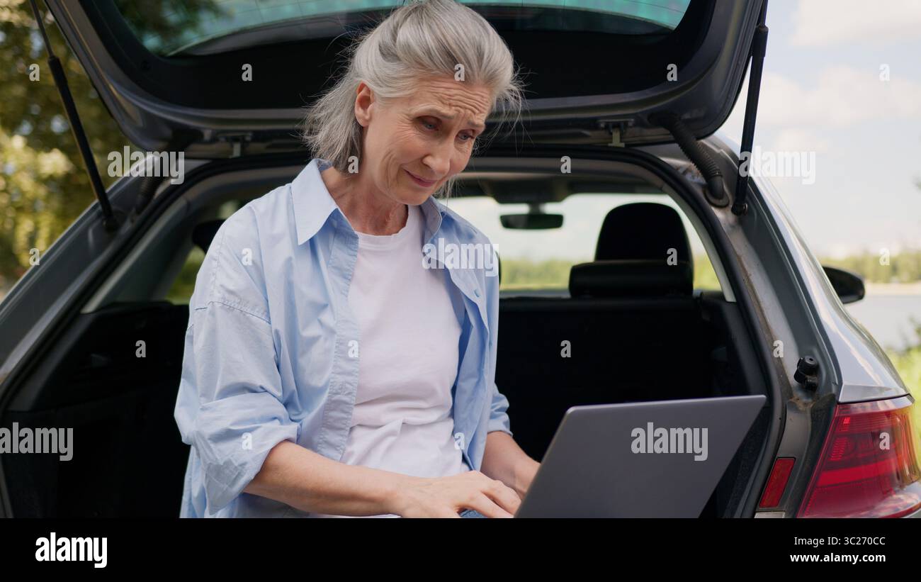 Confus bouleversé caucasien mature femme âgée femme âgée freelance utilisateur SIT voiture coffre d'automobile travaillant en ligne connexion d'ordinateur portable Banque D'Images