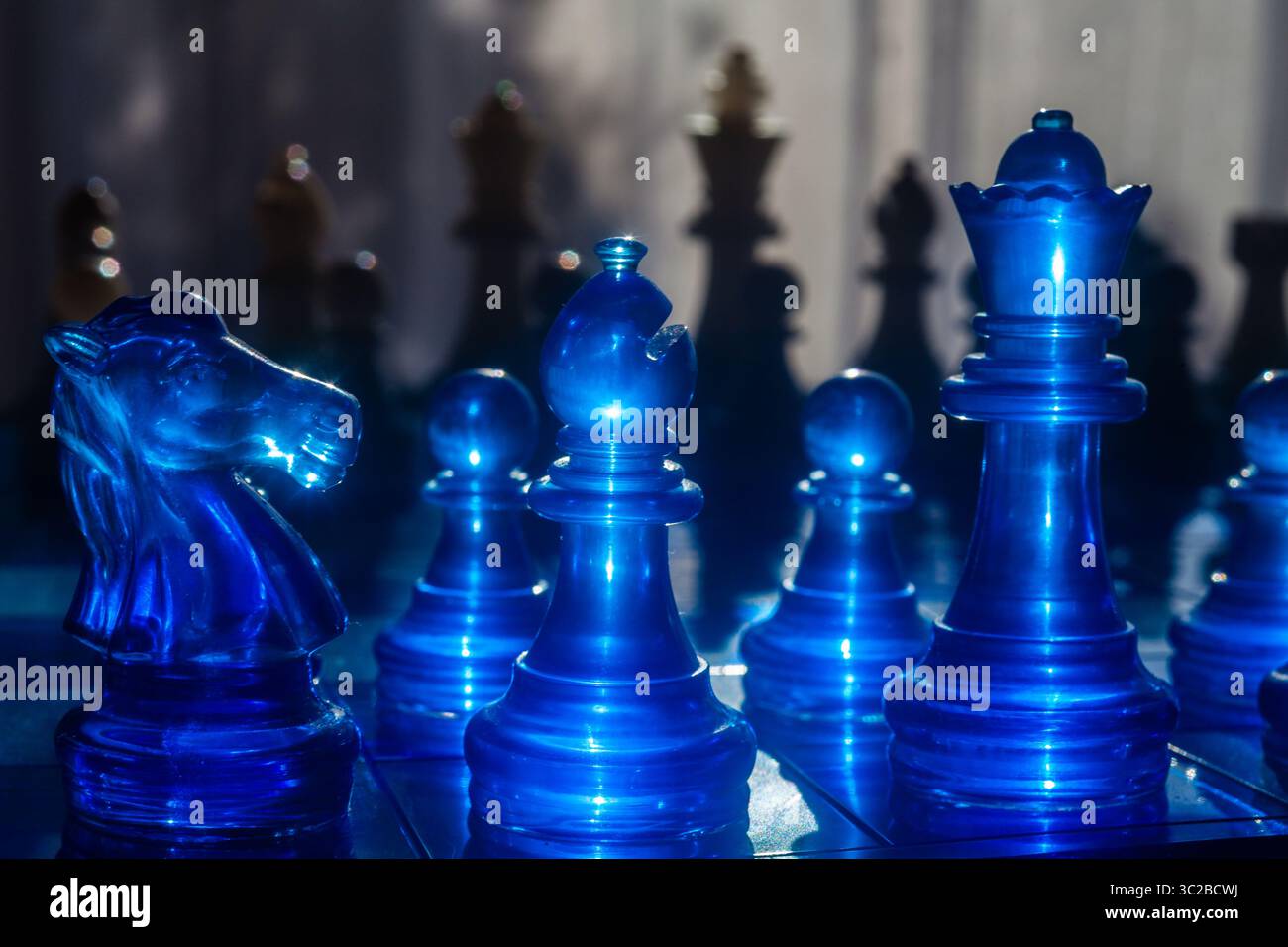 Un arrangement captivant de pièces d'échecs bleues lumineuses, comprenant un cheval (chevalier) et un roi, est présenté sur une surface réfléchissante, avec de la soie dramatique Banque D'Images