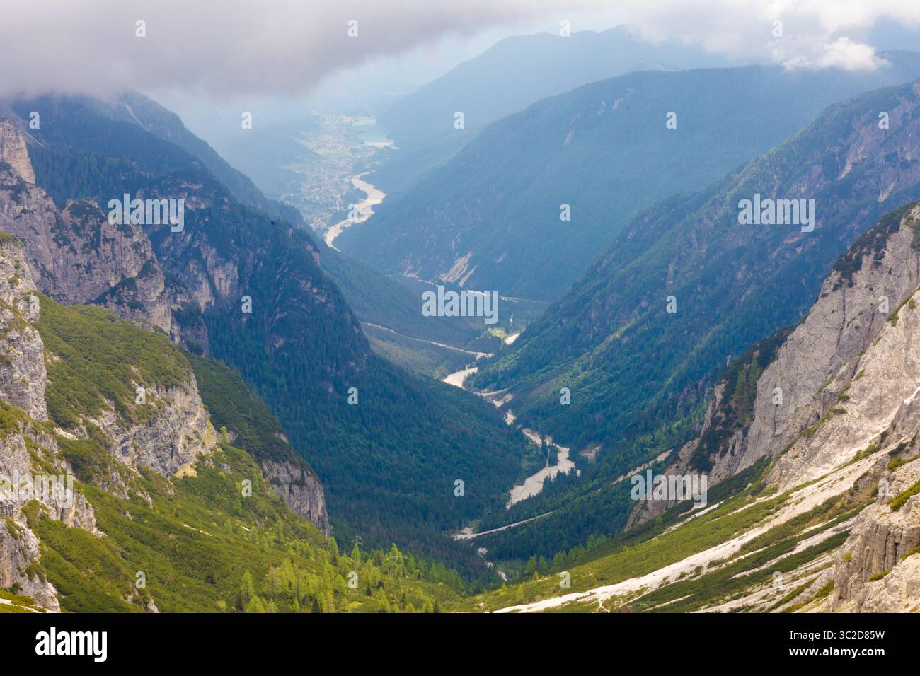 Vue panoramique sur la vallée alpine depuis Tre Cime di Lavaredo, avec rivière sinueuse, forêts luxuriantes, falaises abruptes et nuages bas suspendus. Banque D'Images