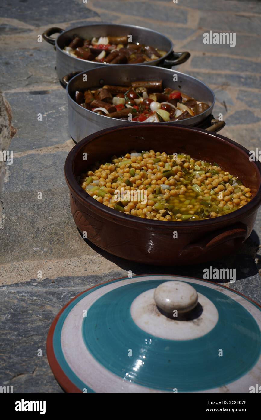 Pot rond en argile rempli de pois chiches mélangés à des poireaux hachés. Deux casseroles en métal en arrière-plan contiennent un ragoût riche avec des morceaux visibles d'aubergines Banque D'Images