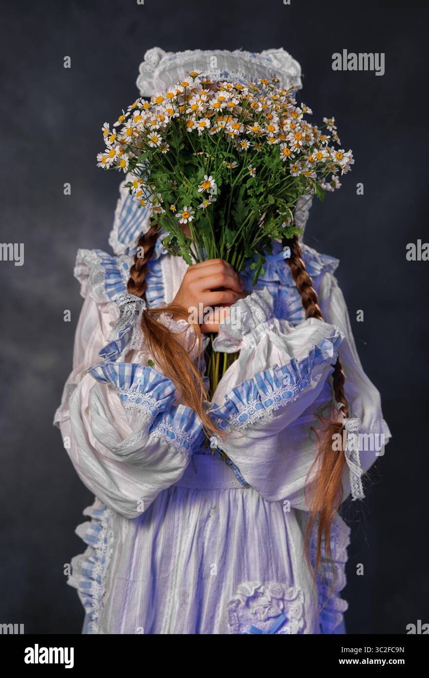 Fille souriante dans la robe vintage tenant un bouquet de marguerites sur fond sombre Banque D'Images