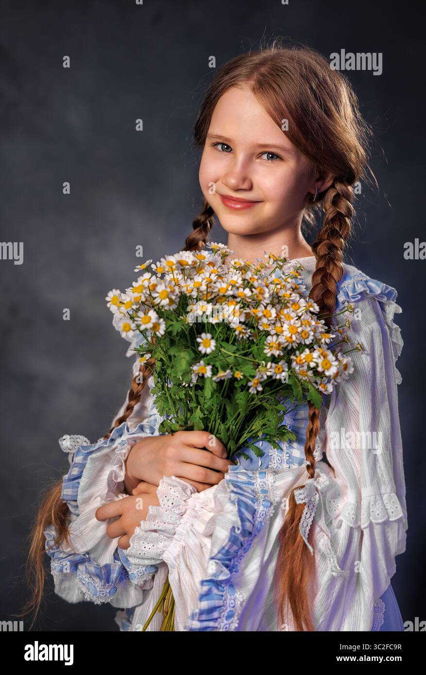 Fille souriante dans la robe vintage tenant un bouquet de marguerites sur fond sombre Banque D'Images