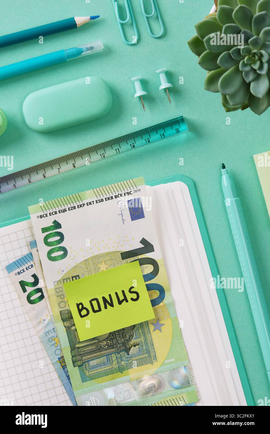 Billets en euros avec un autocollant avec le mot Bonus en anglais couché sur un carnet ouvert. Papeterie de couleur menthe est en arrière-plan. Banque D'Images