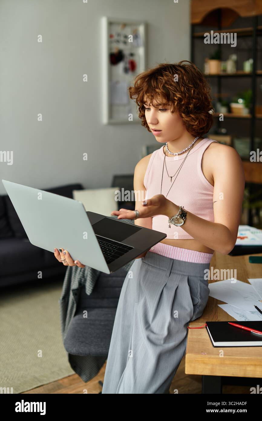 Femme aux cheveux bouclés s'engage avec son ordinateur portable tout en travaillant à la maison dans un appartement élégant. Banque D'Images