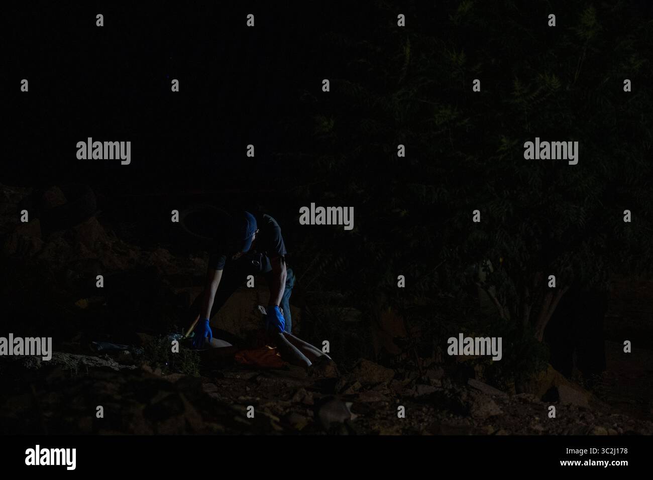 Deux individus naviguent sur un terrain accidenté grâce à une lampe de poche la nuit près d'un plan d'eau à Ciudad Juarez, reflétant les dures réalités de la violence urbaine. Banque D'Images