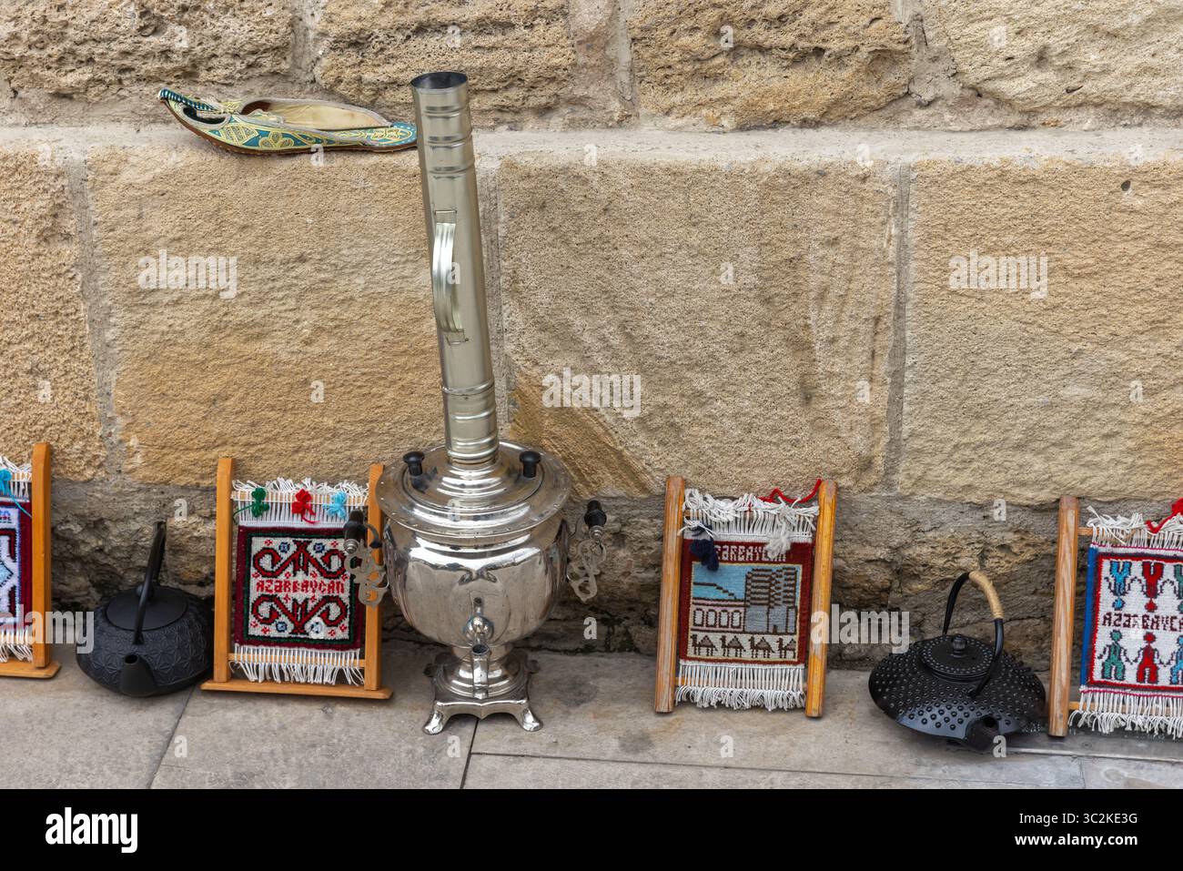 Des objets traditionnels tels qu'un samovar brillant, des textiles tissés artisanaux et des bouilloires rustiques magnifiquement exposées contre un mur de pierre historique à Bak Banque D'Images