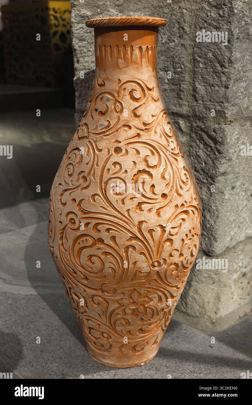 Une vue rapprochée d'un vase en céramique soigneusement décoré avec des motifs floraux détaillés, mis en valeur sur un fond de pierre texturée, mettant en valeur l'artiste Banque D'Images