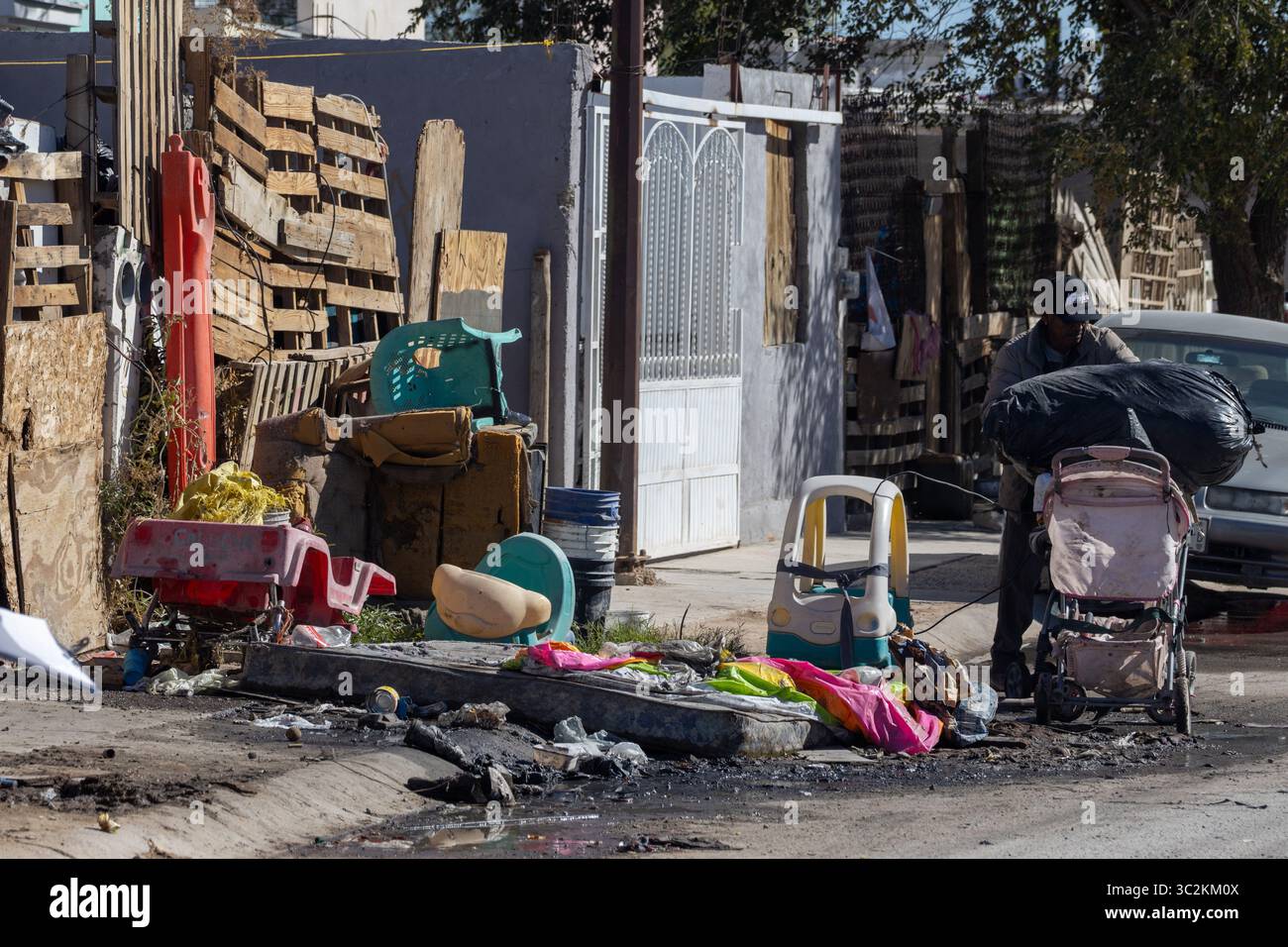 Un homme navigue dans une rue pauvre de Ciudad Juarez, chargé de déchets et d'objets jetés. Banque D'Images