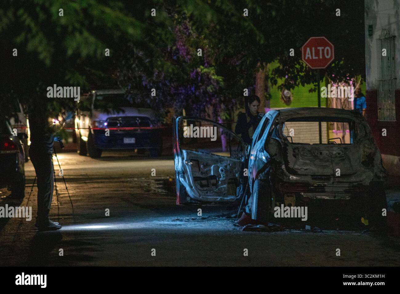 Vue nocturne d'une voiture incendiée à Ciudad Juarez, scène d'une enquête policière en cours dans un contexte de violence urbaine. Banque D'Images