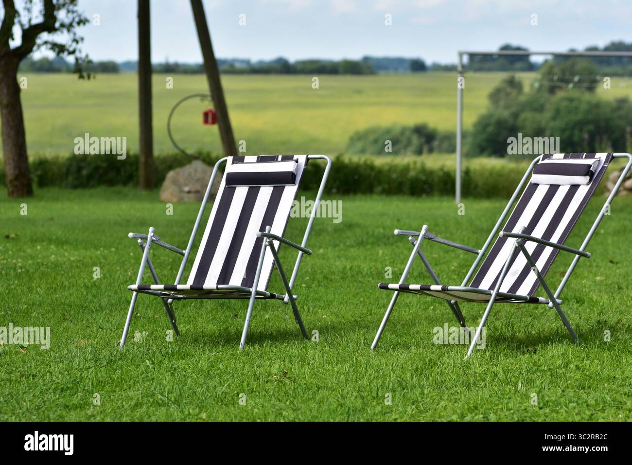 Deux chaises de jardin à rayures noires et blanches sur une pelouse verte vibrante. La disposition des sièges extérieurs évoque la détente estivale, les loisirs et l'atmosphère confortable du jardin Banque D'Images