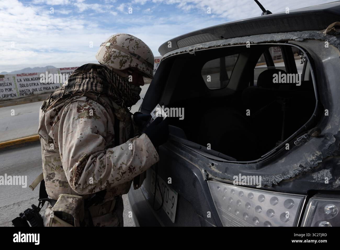 Soldat inspecte un véhicule endommagé à Ciudad Juarez, sur fond de slogans anti-violence. Banque D'Images