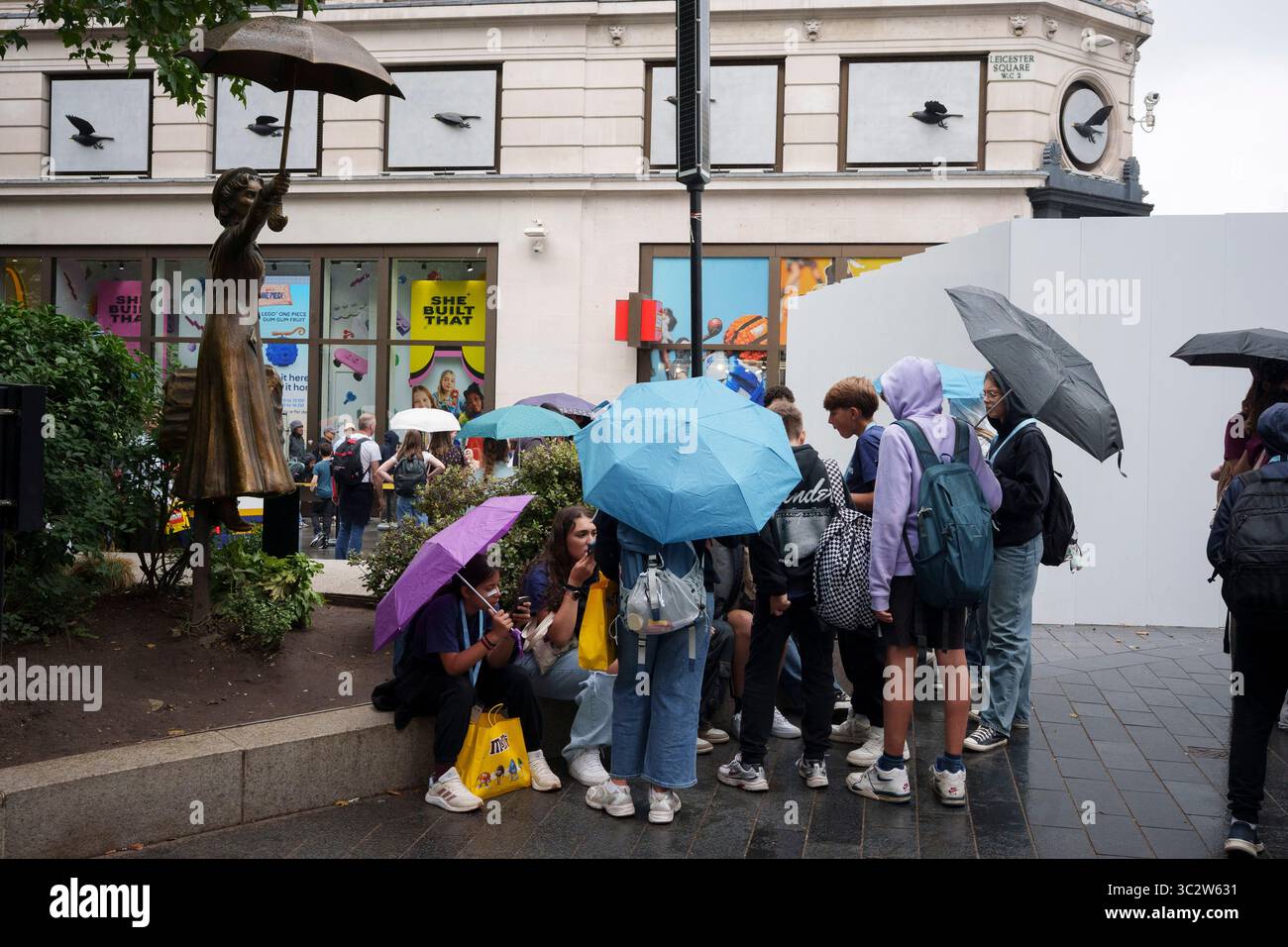 Londoniens et visiteurs de la capitale endurent un après-midi humide à Leicester Square où la statue de Mary Poppins est située portant son propre parapluie, le 24 juillet 2025, à Londres, en Angleterre. Banque D'Images