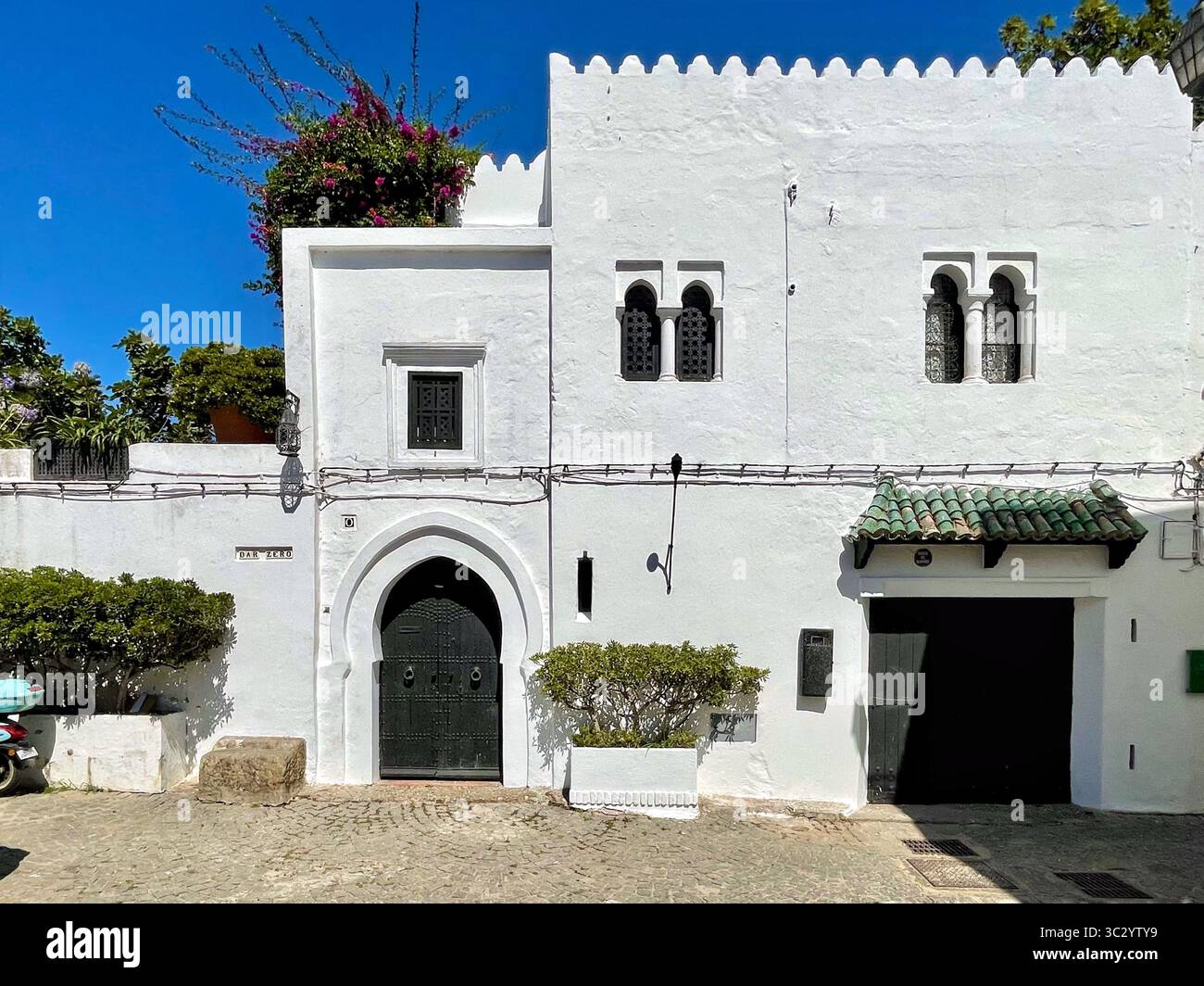 Extérieur d'une maison marocaine traditionnelle dans la médina historique de Tanger, avec murs blanchis à la chaux, fenêtres cintrées et texture vieillie. Banque D'Images