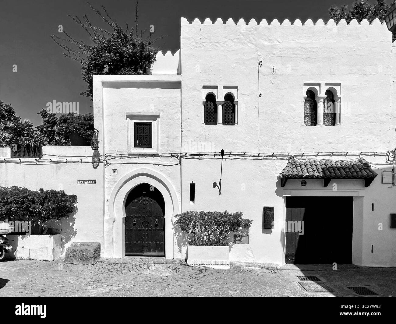 Extérieur d'une maison marocaine traditionnelle dans la médina historique de Tanger, avec murs blanchis à la chaux, fenêtres cintrées et texture vieillie. Banque D'Images