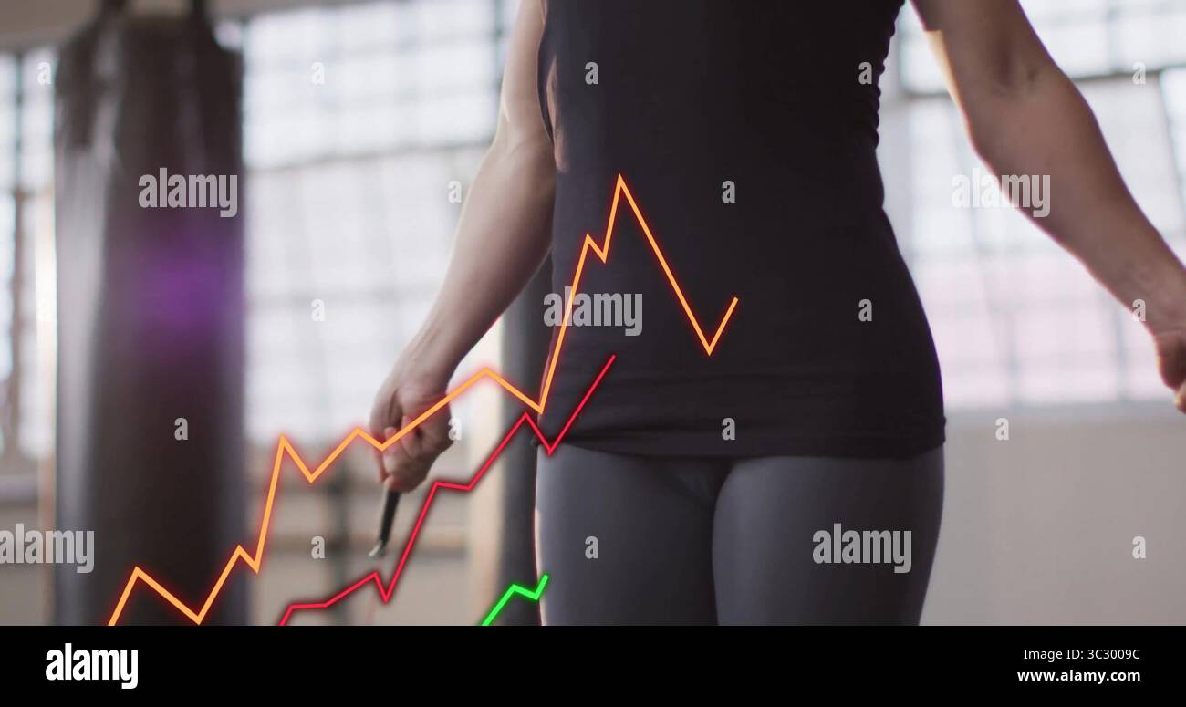 Femme en vêtements d'activité noirs tenant des poignées de corde à sauter dans le gymnase, avec sac de poinçonnage et superpositions de graphique Banque D'Images