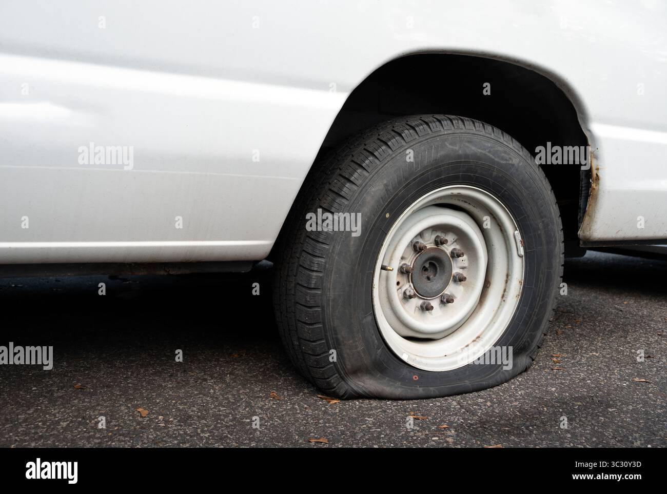 Main tenant un téléphone avec un écran blanc vierge, idéal pour une utilisation maquette ; Un pneu de voiture plat est vu en arrière-plan, parfait pour illustrer le service automobile Banque D'Images