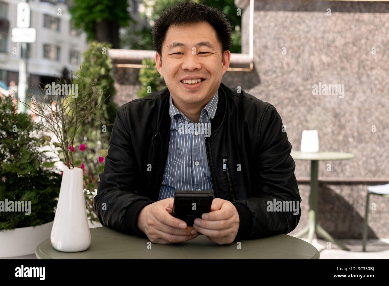 Homme asiatique souriant à la caméra tout en tenant un smartphone Banque D'Images