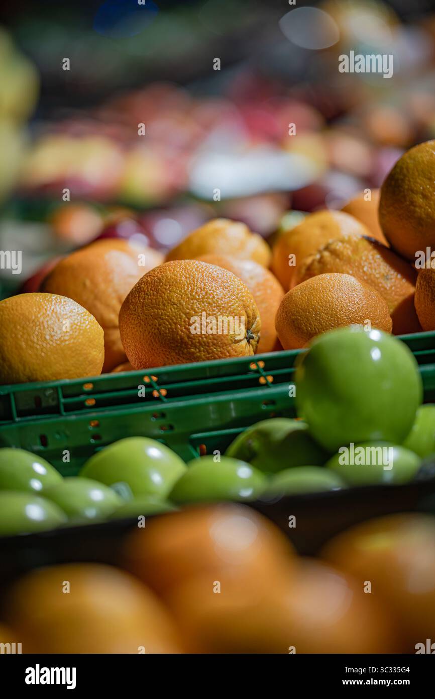 Gros plan détaillé de pommes vertes et d'oranges empilées dans des caisses en plastique dans un marché ou une épicerie. L'accent est mis sur une pomme verte brillante. Banque D'Images