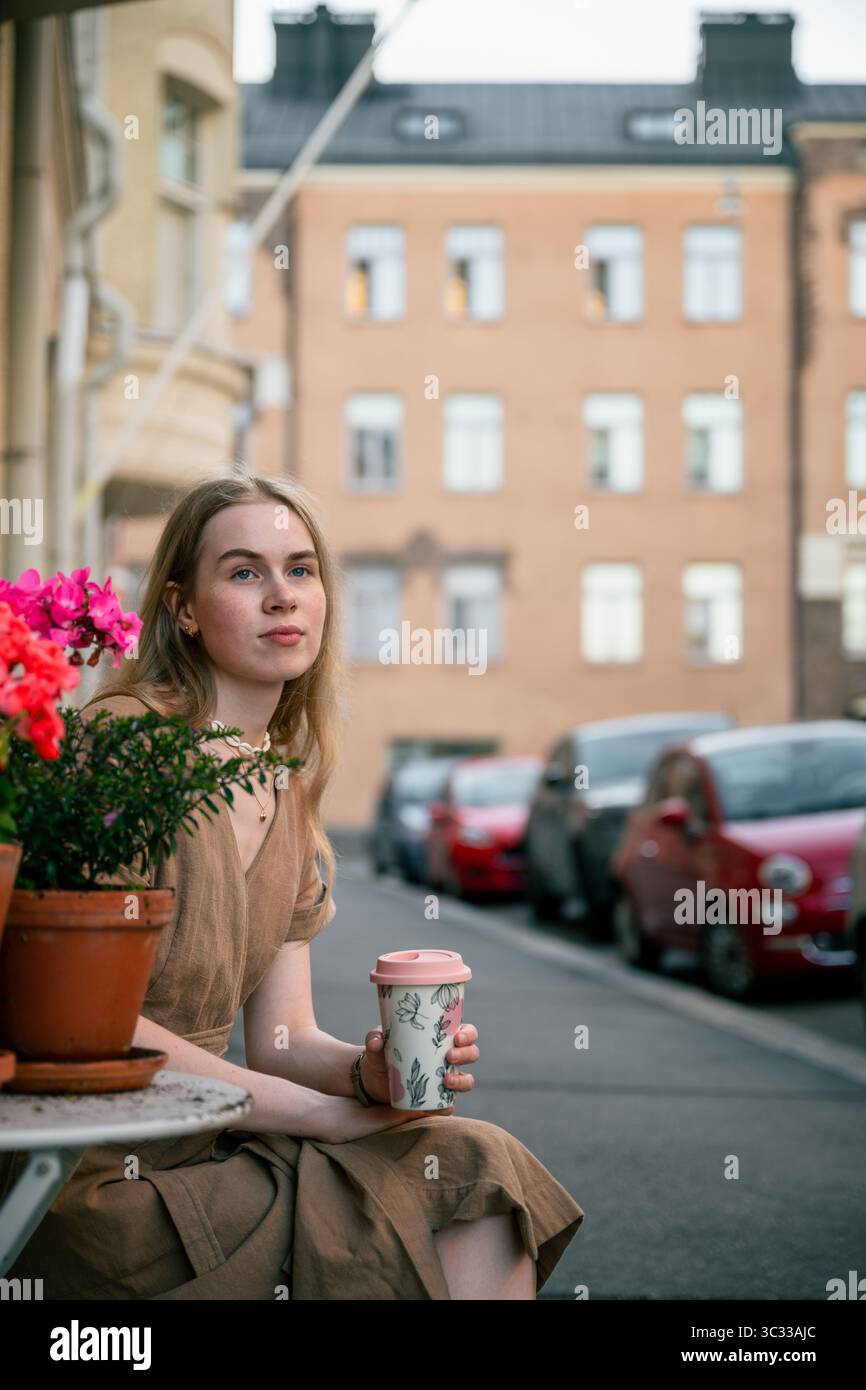 Jeune femme assise avec une tasse de café sur la rue de la ville dans la soirée d'été Banque D'Images