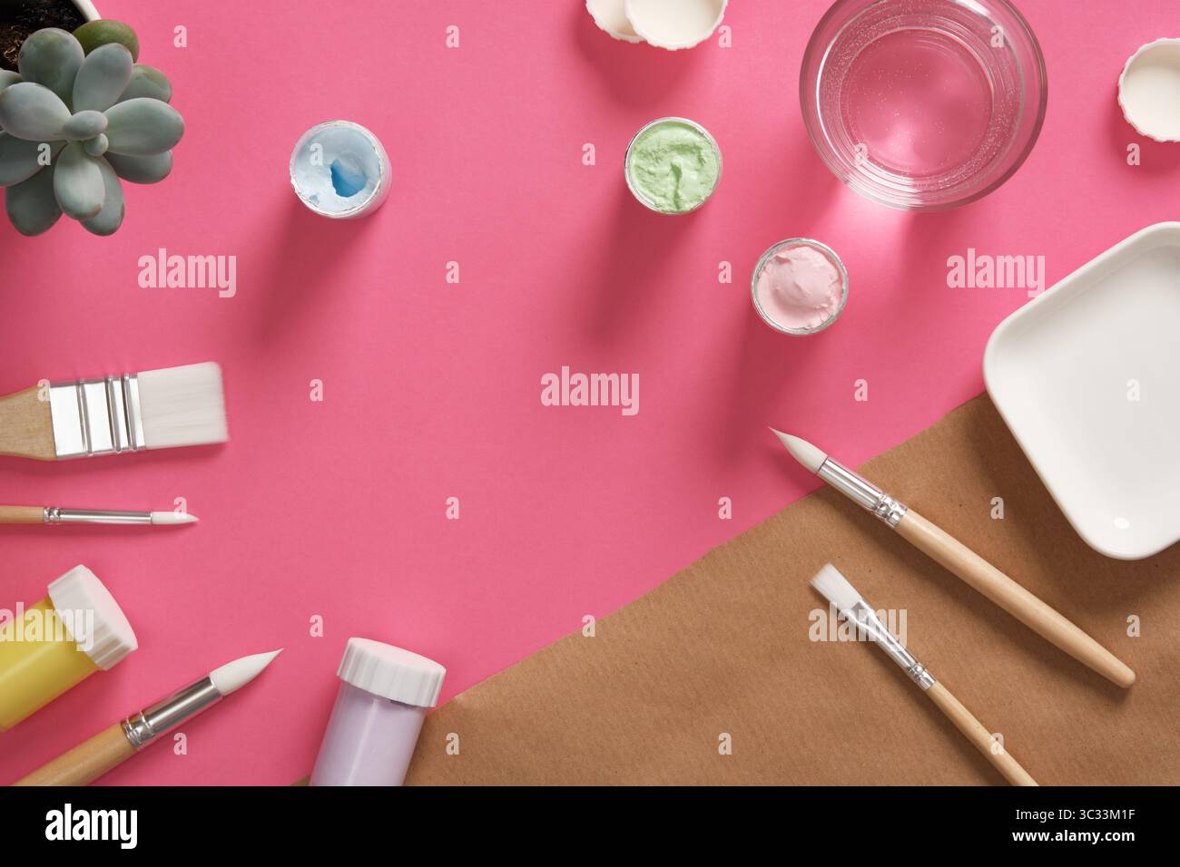 Préparation pour la peinture. Pots de gouache, pinceaux, un verre d'eau sur fond rose. Un endroit pour votre texte. Banque D'Images