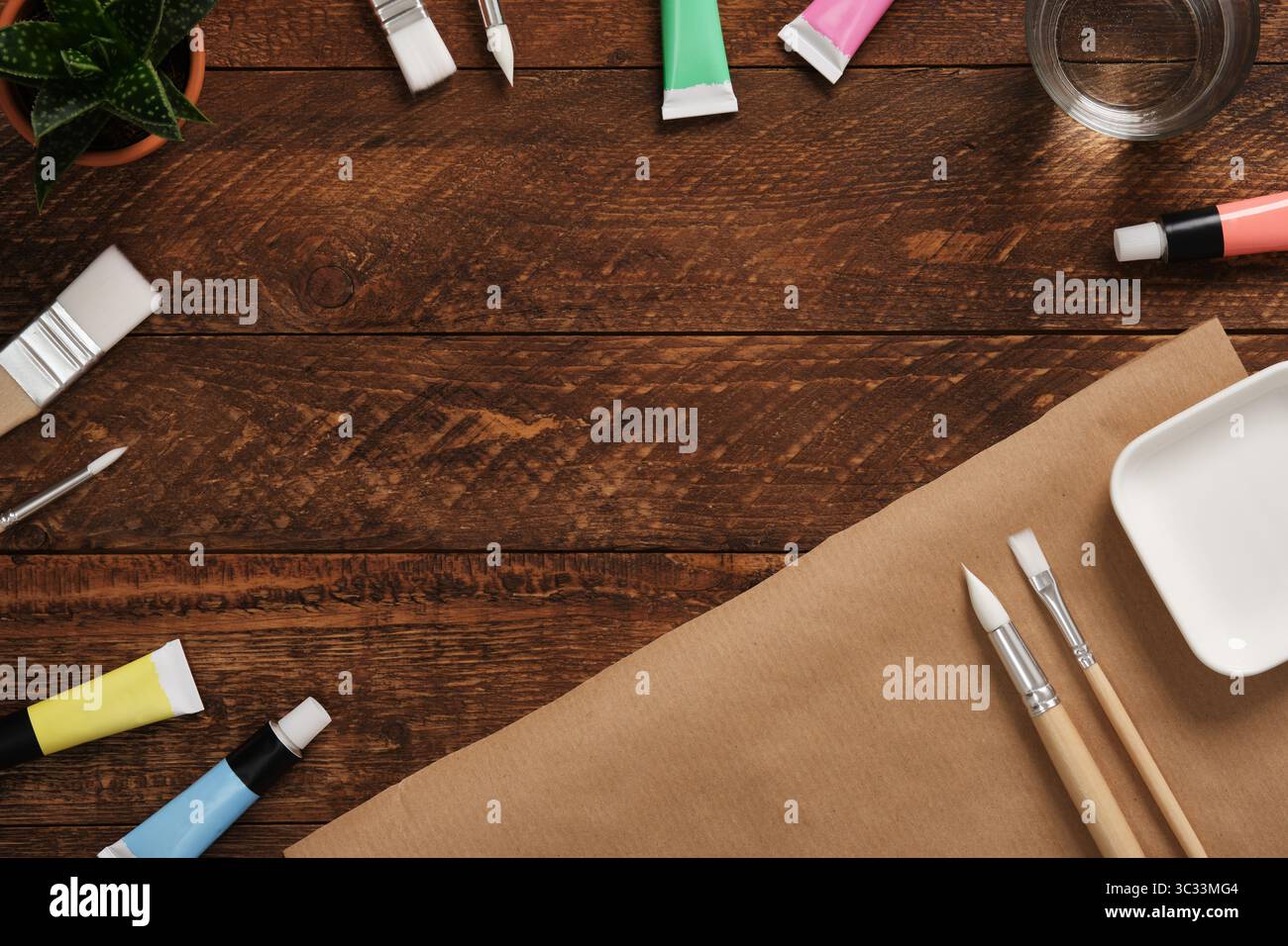 Préparation pour la peinture. Tubes avec des peintures acryliques, des pinceaux, un verre avec de l'eau sur un fond en bois foncé. Place pour le texte. Banque D'Images