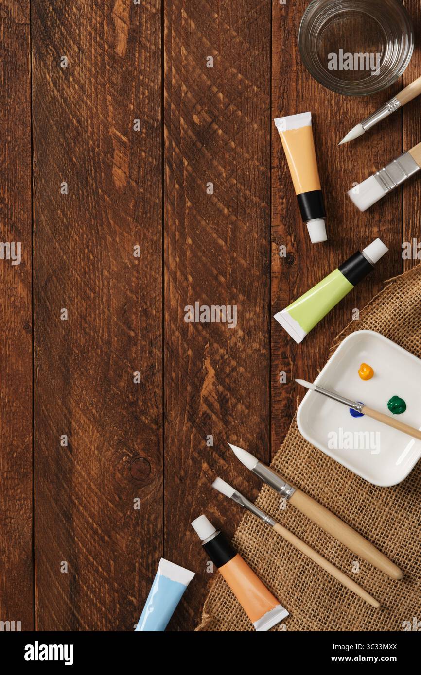 Préparation pour la peinture. Tubes avec des peintures acryliques, des pinceaux, un verre avec de l'eau sur un fond en bois foncé. Place pour le texte. Banque D'Images