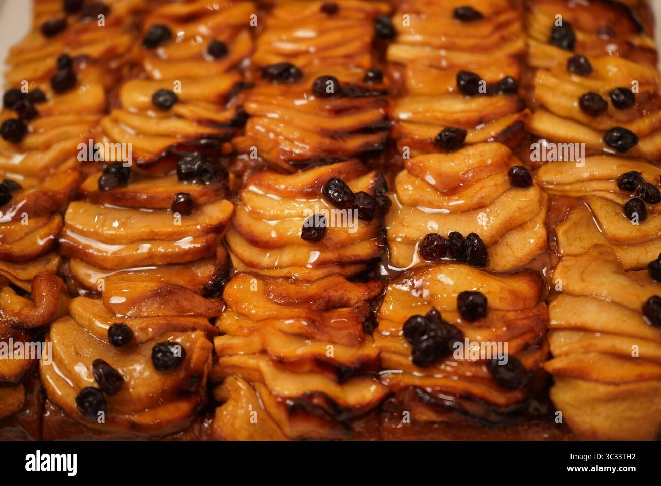 Gros plan de tranches de tarte aux pommes glacées recouvertes de raisins secs soigneusement disposés en quadrillage. La tarte présente des tranches de pomme marron doré, caramélisées Banque D'Images