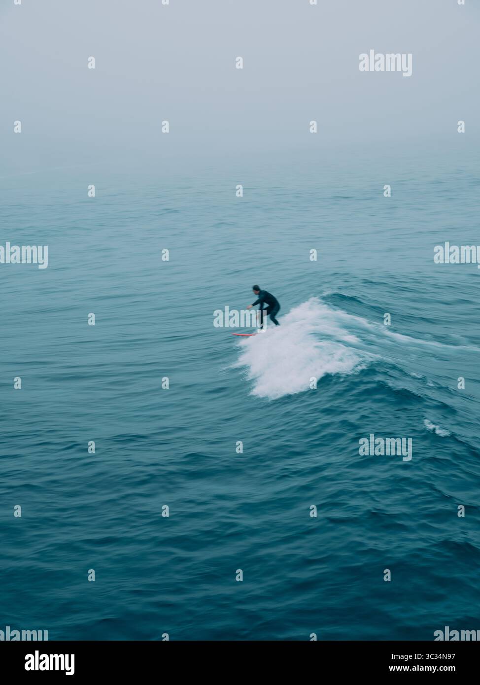 Une figure de surfeur floue solitaire perdue parmi les vagues dans un paysage marin bleu avec du mouvement Banque D'Images