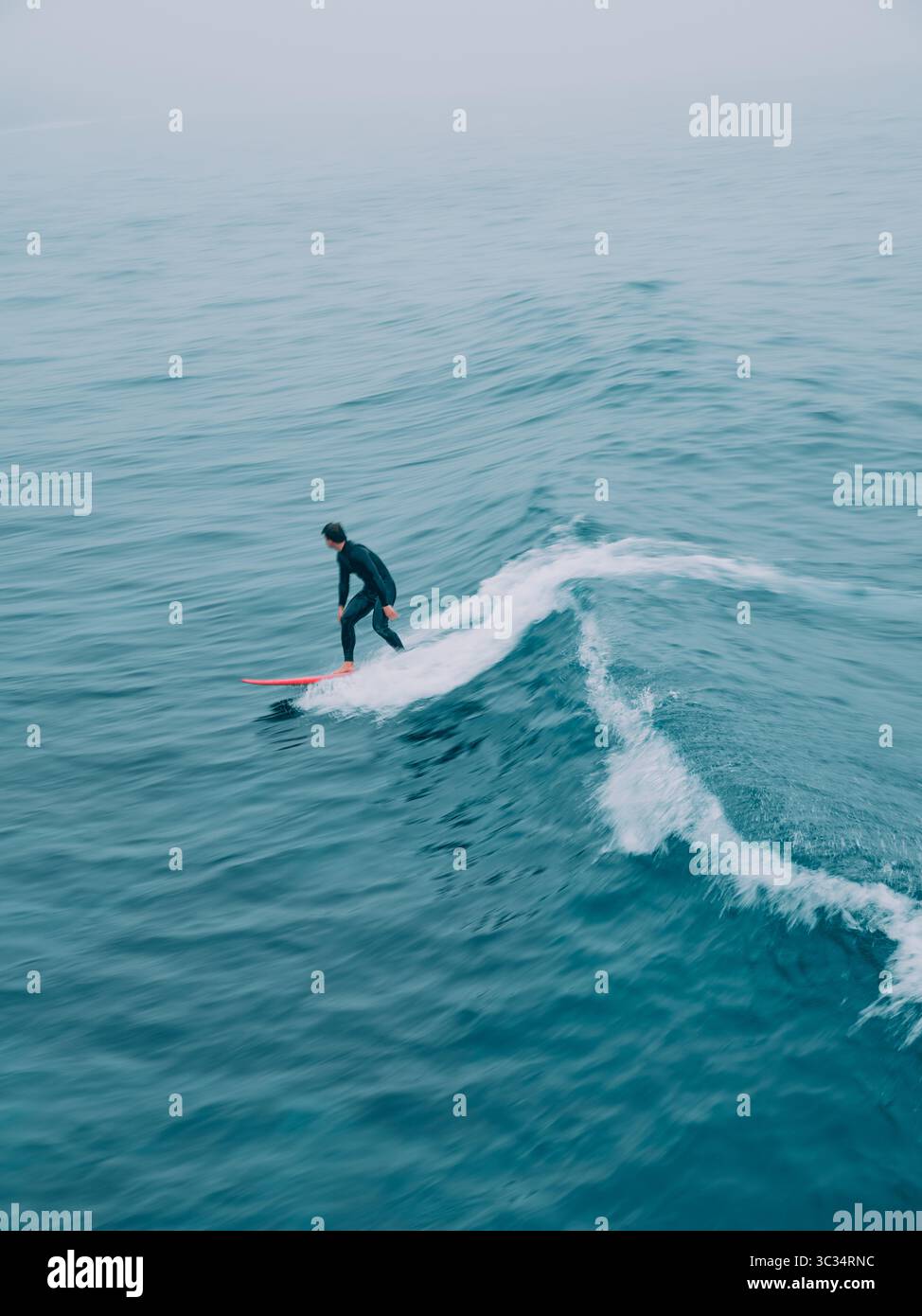 Une figure de surfeur floue solitaire perdue parmi les vagues dans un paysage marin bleu avec du mouvement Banque D'Images