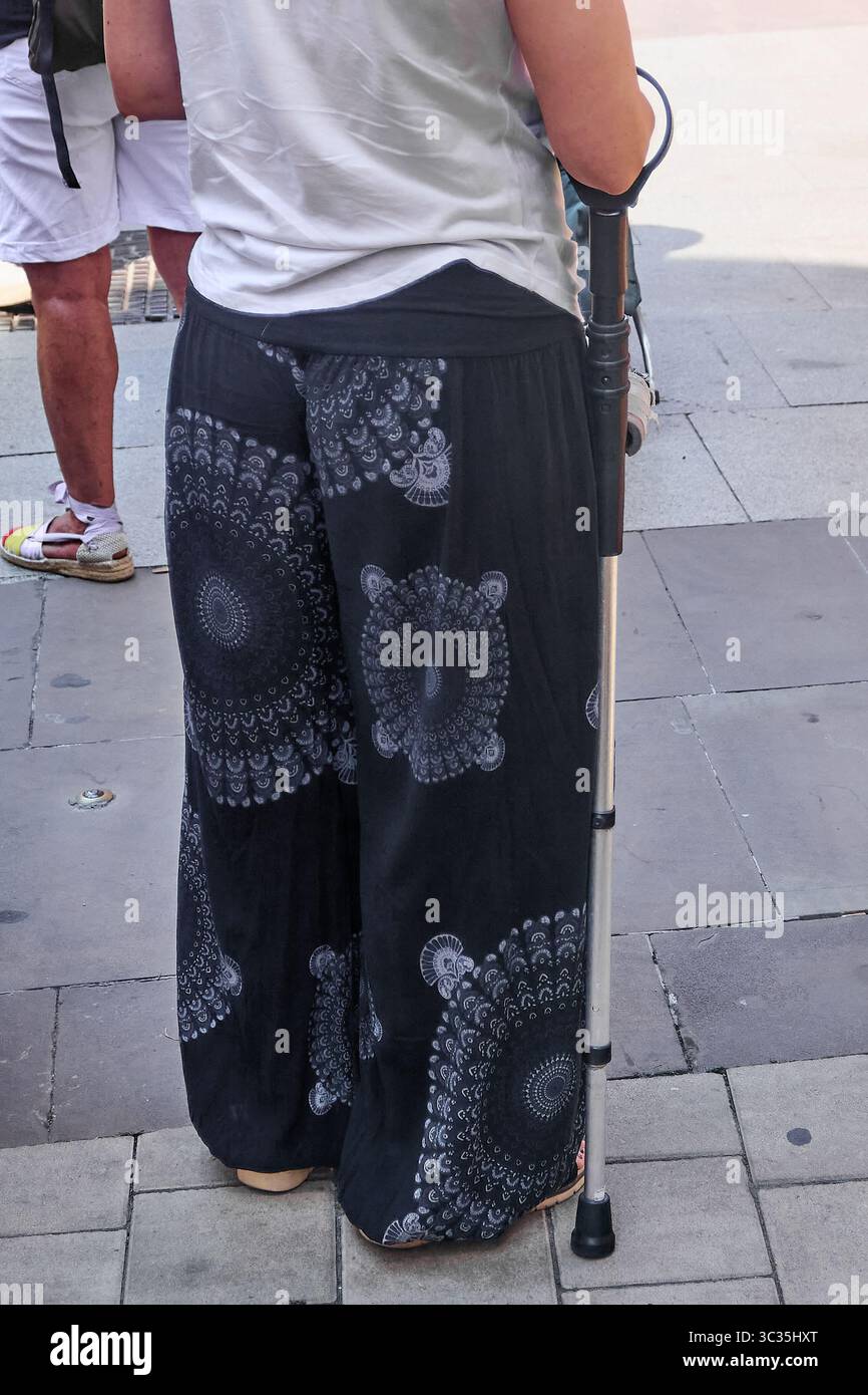 Une femme solitaire utilisant une aide à la mobilité sur un trottoir urbain au soleil. Idéal pour la santé, le soutien et le déplacement gracieux dans les environnements urbains. Banque D'Images