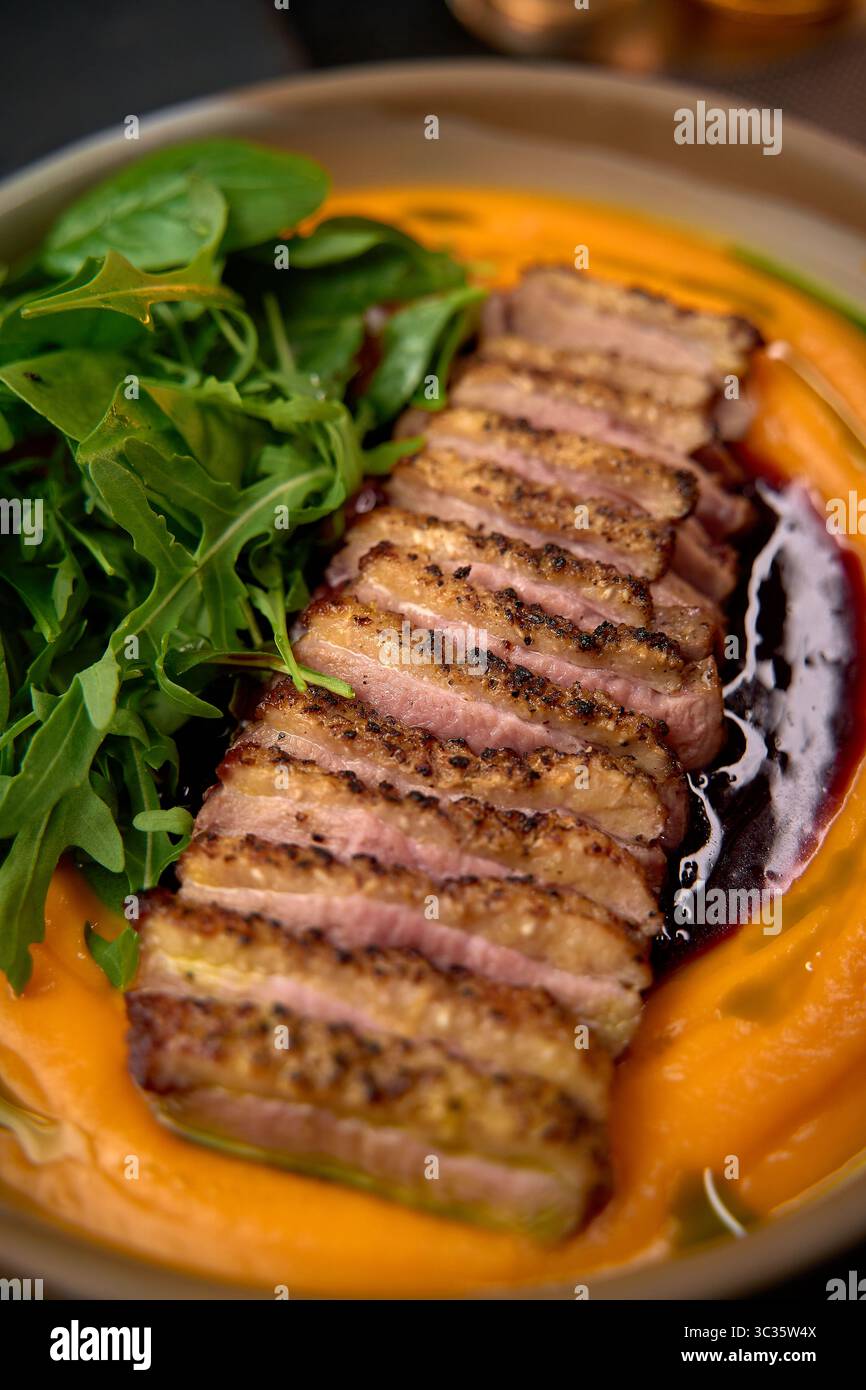 Magret de canard délicieusement grillé servi sur un lit de purée de patates douces et crémeuses accompagné de légumes verts frais pour une sensation gustative Banque D'Images