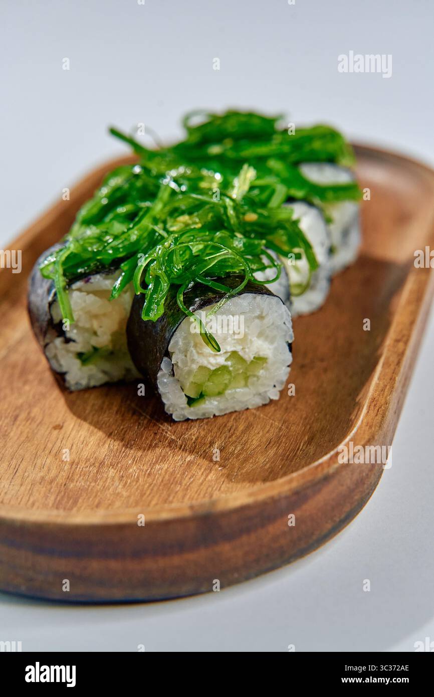 Délicieux Sushi Rolls composés d'ingrédients frais recouverts d'algues vives sur une assiette en bois naturel pour un délice culinaire Banque D'Images