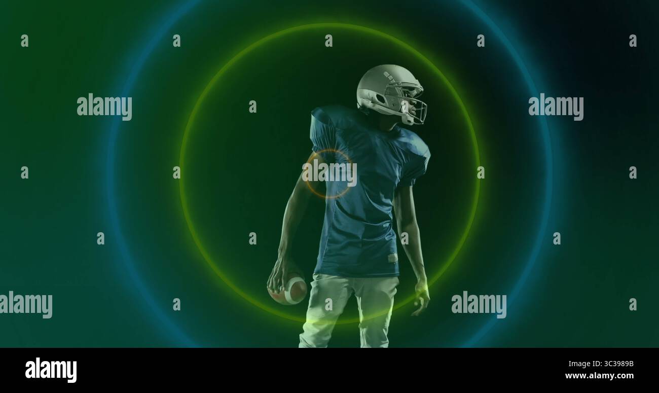 Joueur de football tenant le football, portant un casque, maillot avec un pantalon en studio avec des anneaux néon Banque D'Images