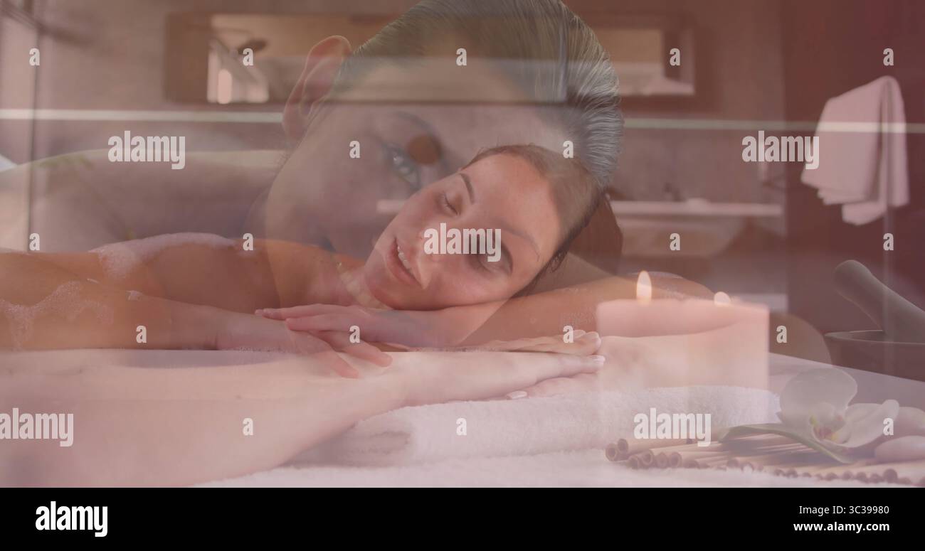 Femme recevant un massage dans la salle de soins spa, avec table drapée de serviettes blanches et bougie allumée Banque D'Images Femme recevant un massage dans la salle de soins spa, avec table drapée de serviettes blanches et bougie allumée Banque D'Images