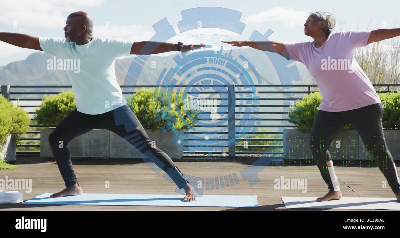 Couple pratiquant portant des vêtements de sport exécutant Warrior II pose sur la terrasse, avec interface numérique Banque D'Images Couple pratiquant portant des vêtements de sport exécutant Warrior II pose sur la terrasse, avec interface numérique Banque D'Images